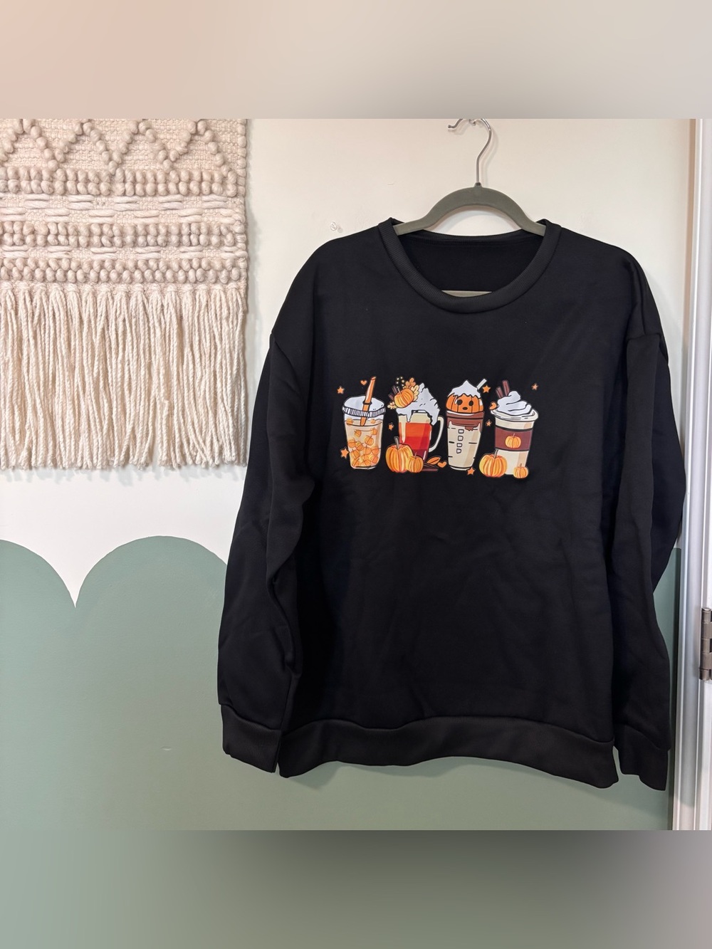 Black crewneck sweatshirt with graphic of four autumn-themed drinks with pumpkin